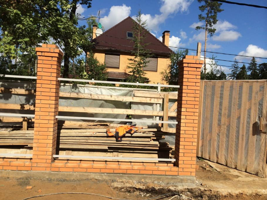 Деревянный забор между кирпичными столбами